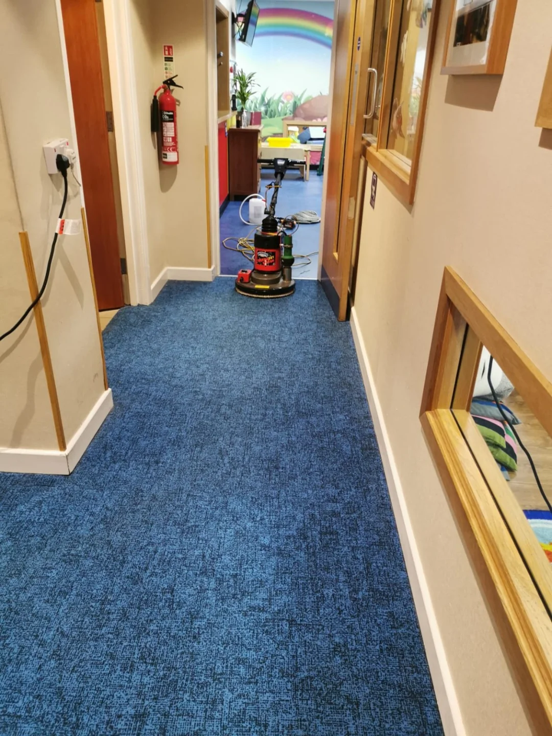 Carpet cleaning machine on a blue corridor carpet beside wooden doors