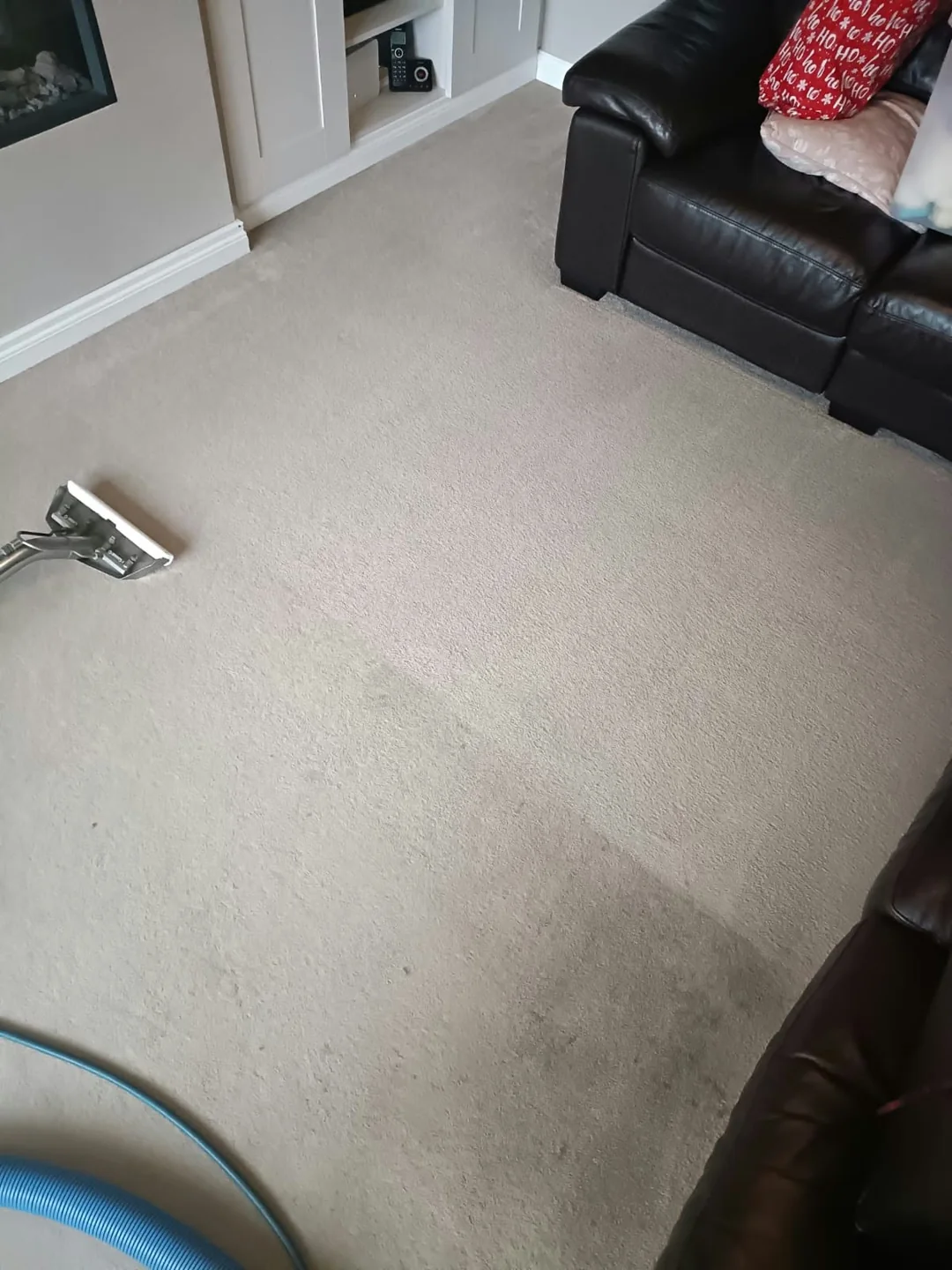 Cleaning wand on a light living-room carpet beside a black sofa